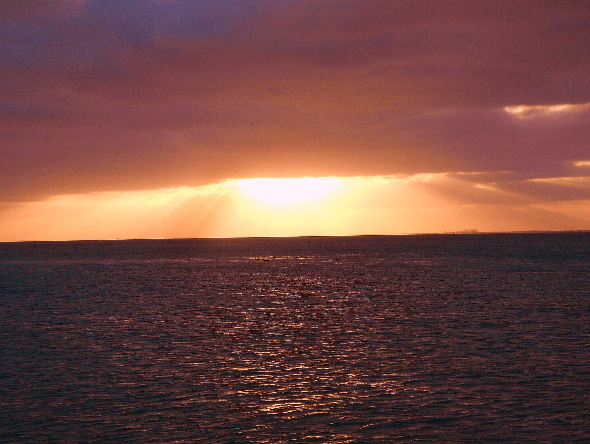 The sun going down behind cloud over the flat water of Biscayne Bay