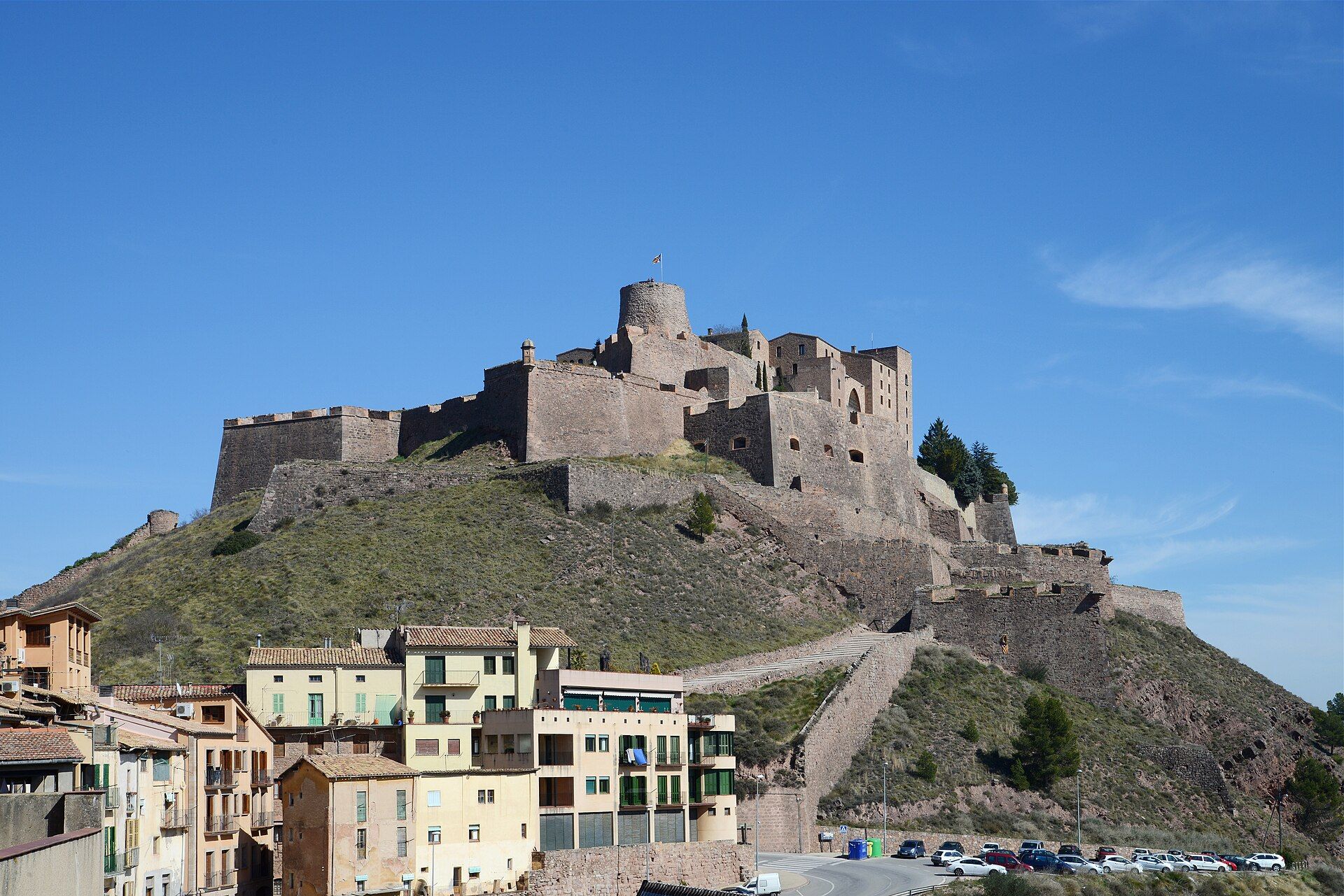 Cardona castle and its stone ramparts on top of a grassy hill, with town houses at the foot