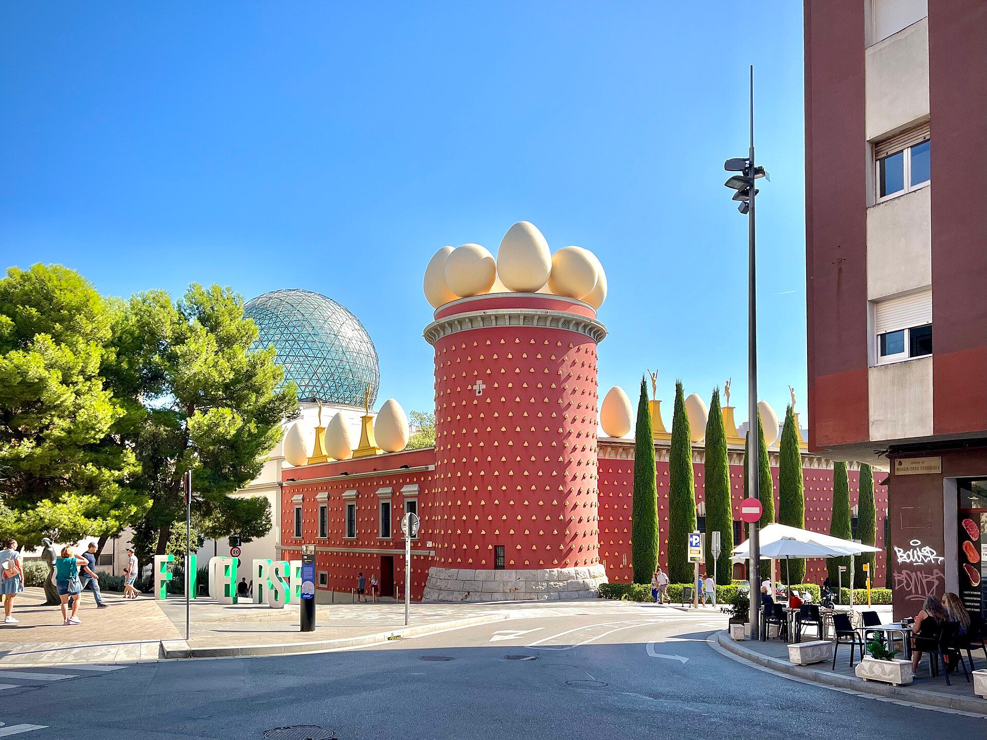 The red Torre Galatea of the Dalí Theatre-Museum in Figueres, topped with giant eggs, with the glass dome behind it