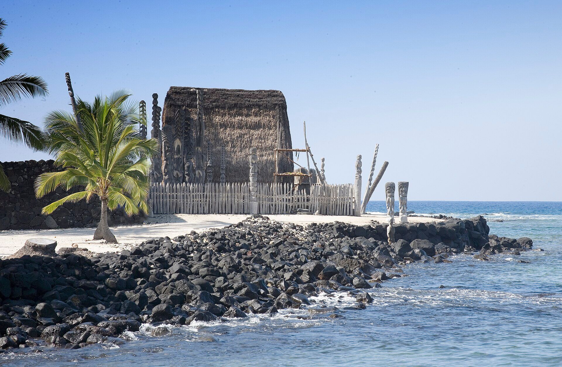Carved wooden kiʻi and a thatched temple on the lava point at Puʻuhonua o Hōnaunau