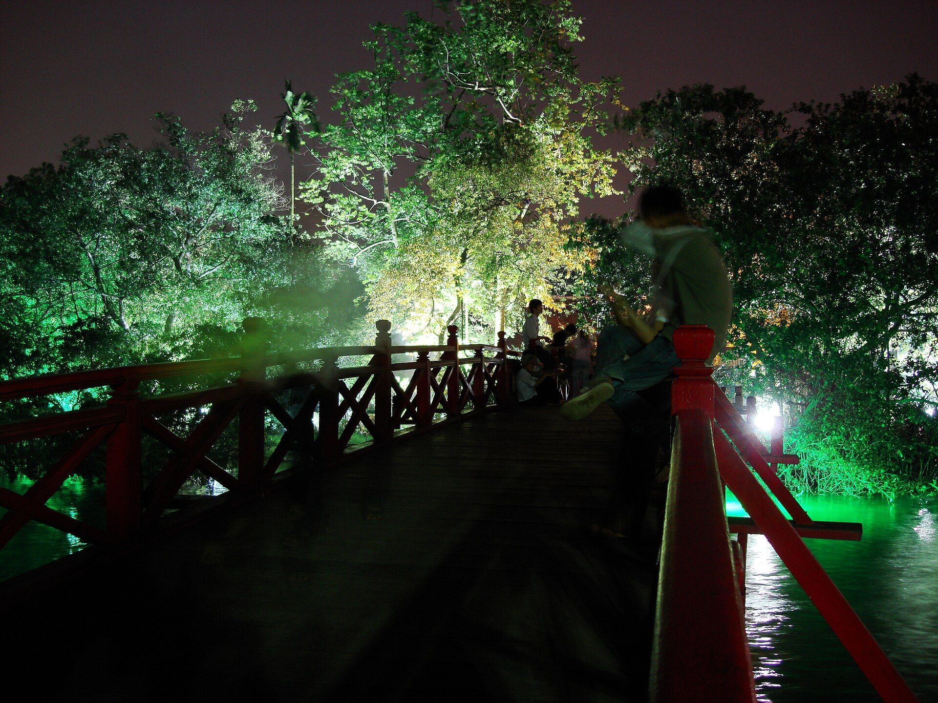 The red Huc bridge to Ngoc Son Temple lit up at night among trees