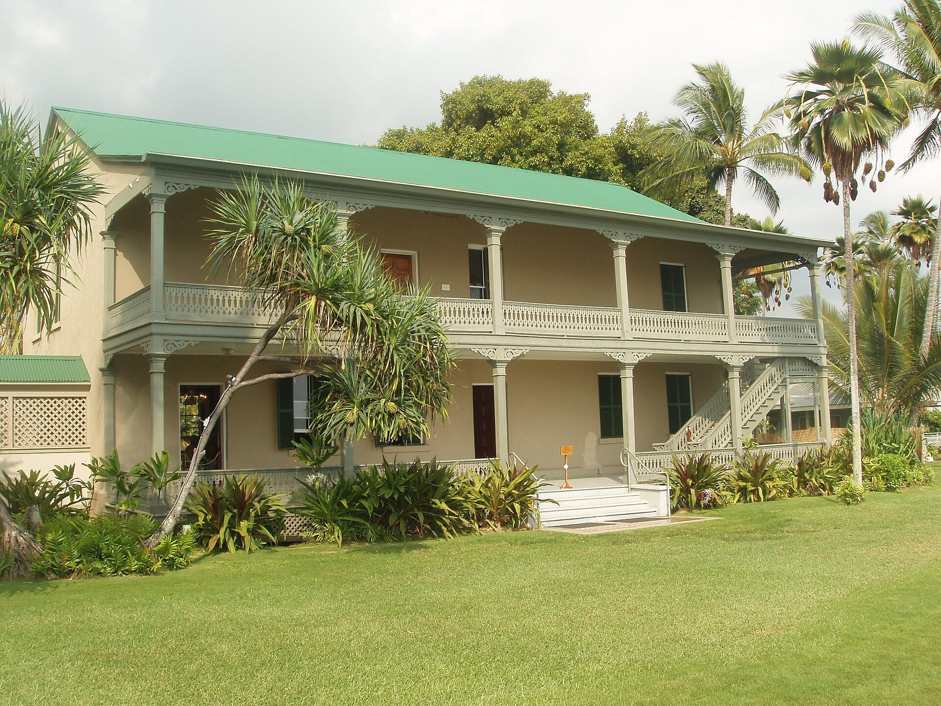 The two-storey veranda of Huliheʻe Palace behind a lawn and palms