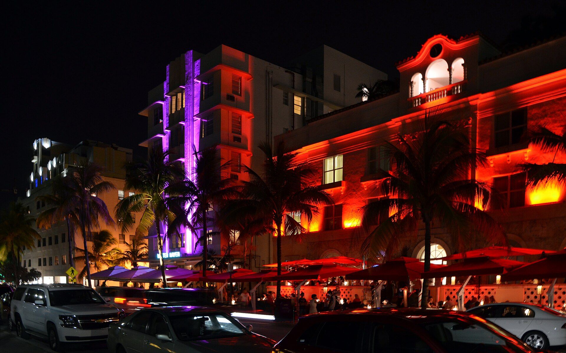 Art Deco hotels on Ocean Drive lit orange and purple at night, with palms along the street