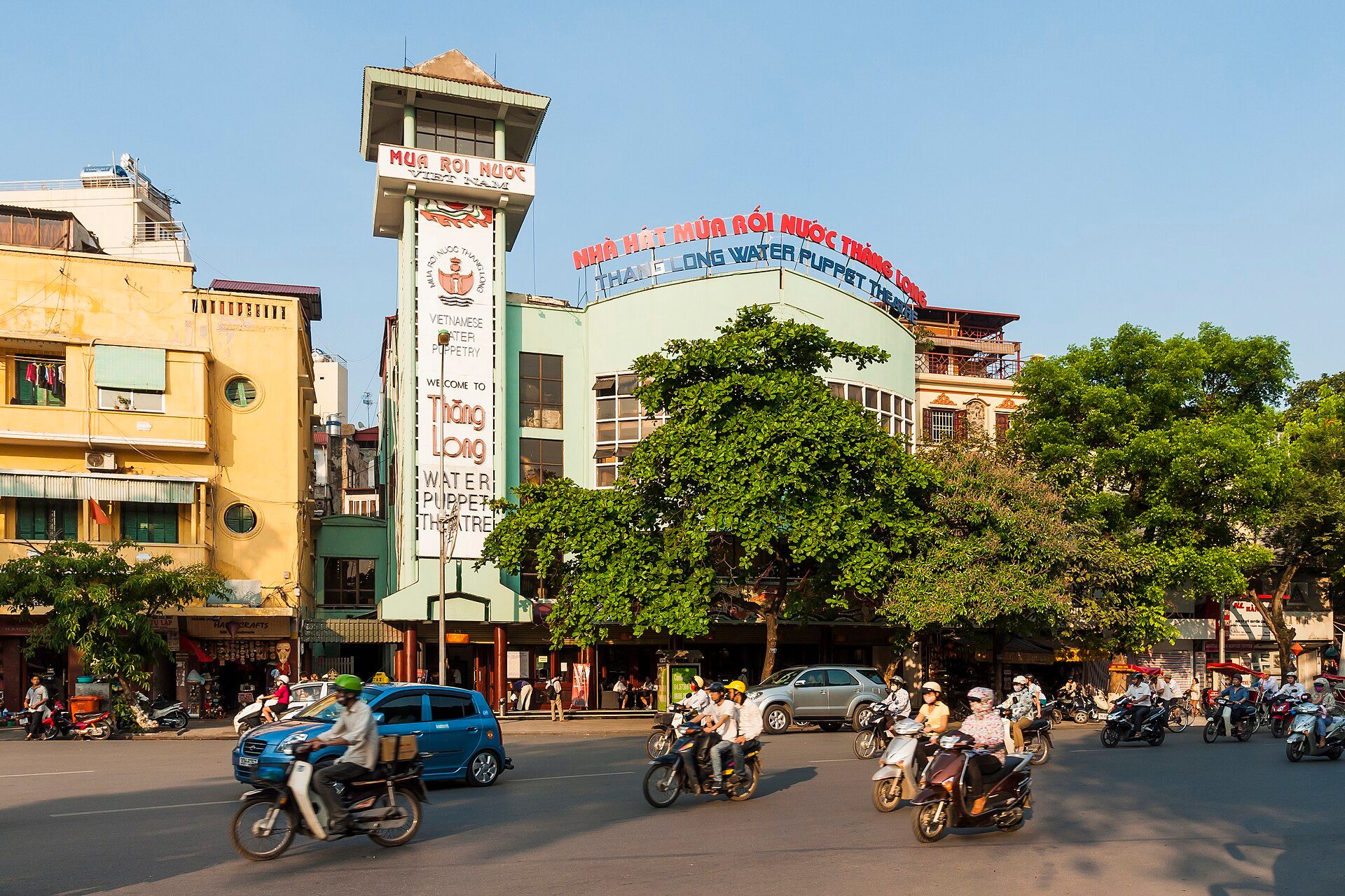 The Thang Long Water Puppet Theatre on a busy corner with scooters passing