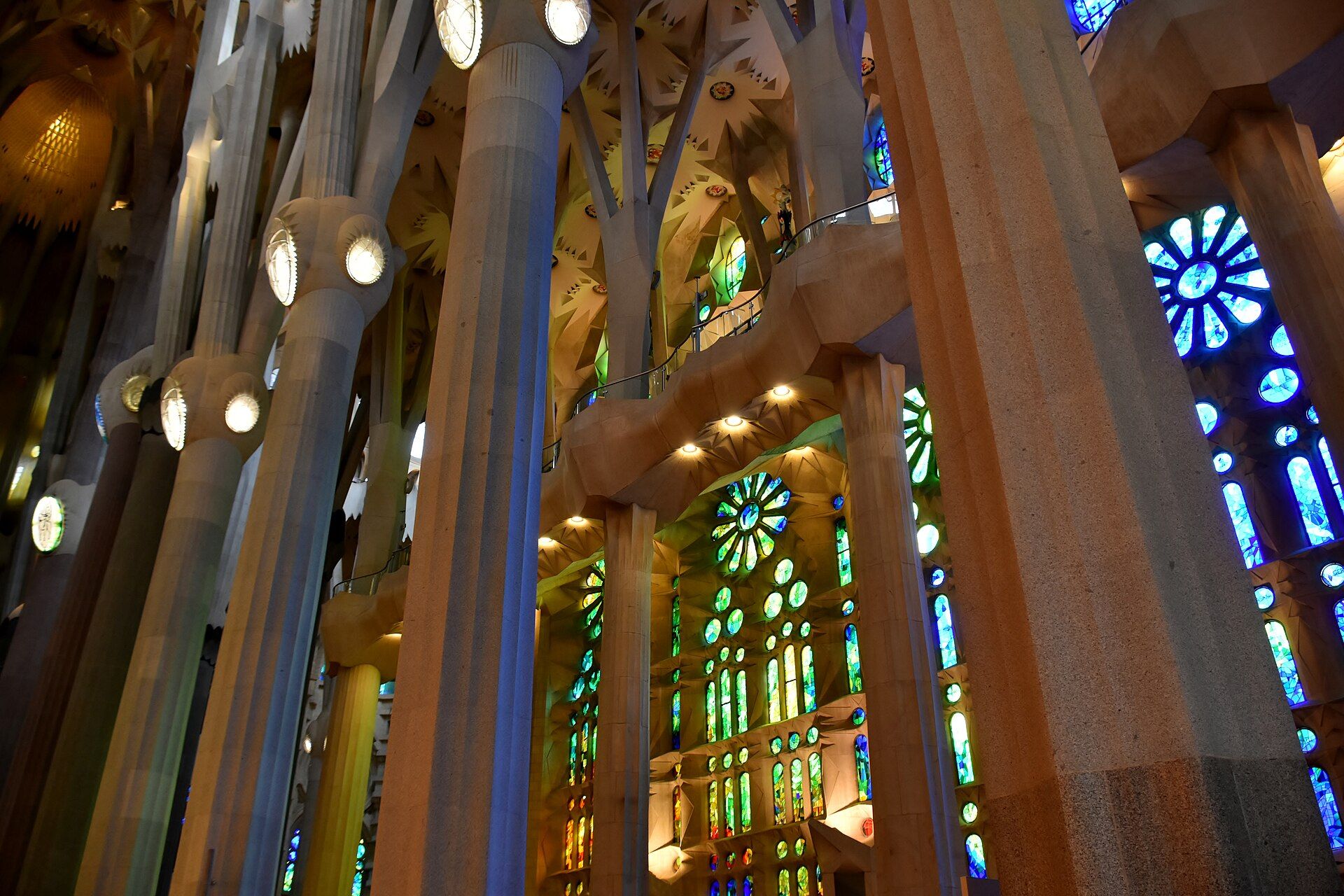 Branching stone columns inside the Sagrada Família, lit green and blue by the stained glass windows