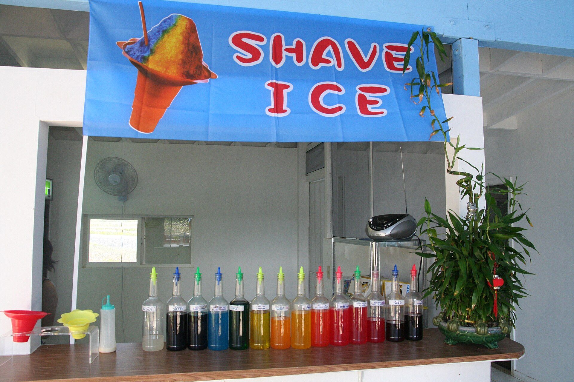 A shave ice stand with a row of bright syrup bottles on the counter