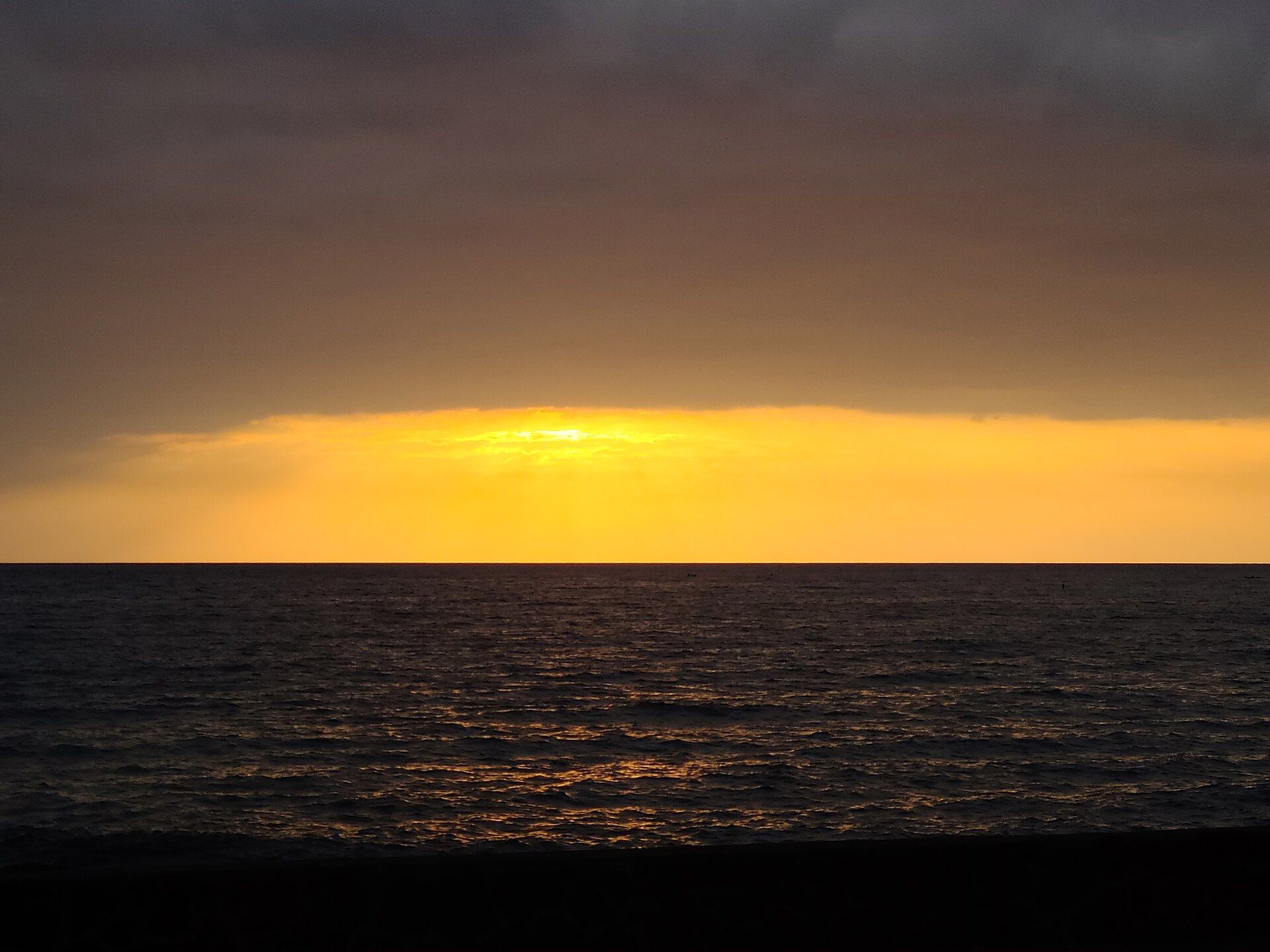The sun setting into a flat sea off Kailua-Kona under a band of cloud