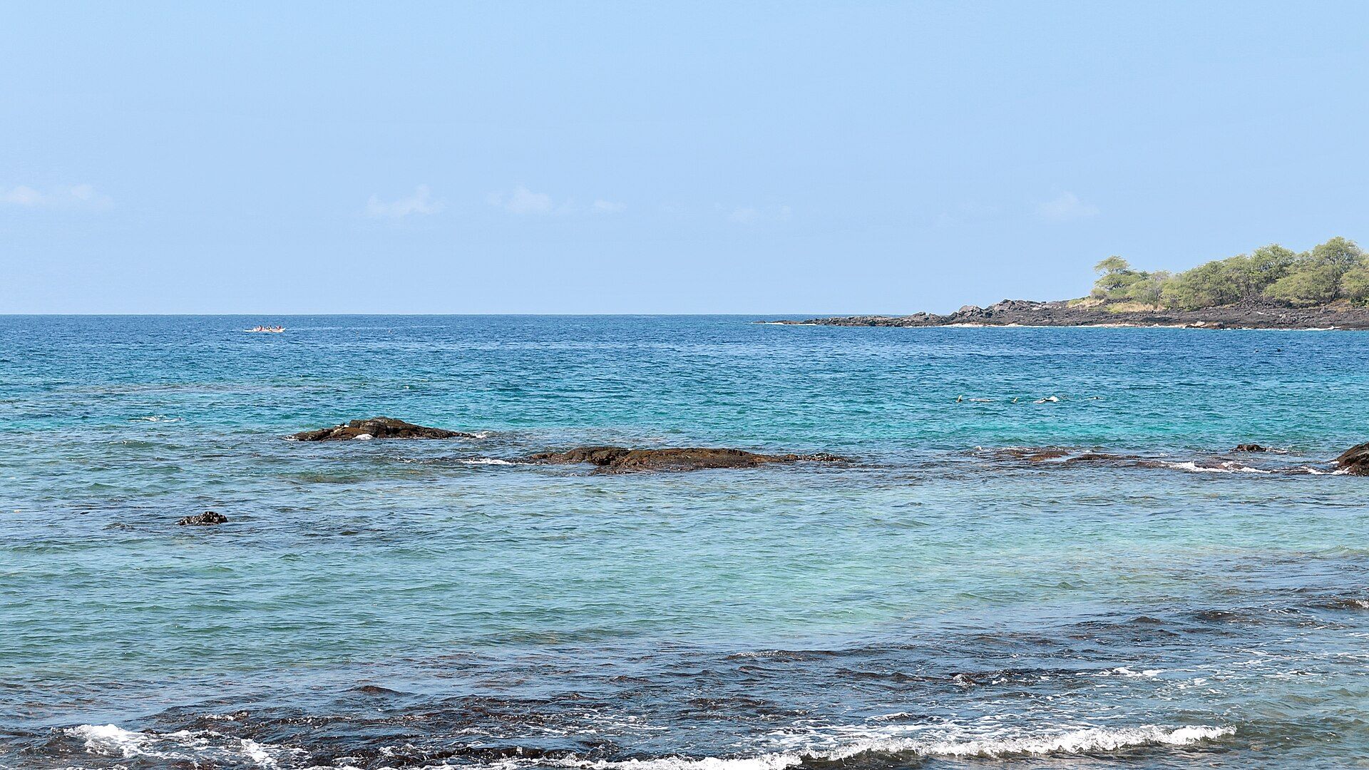 Clear blue water over dark lava rock at Hōnaunau Bay under a bright sky