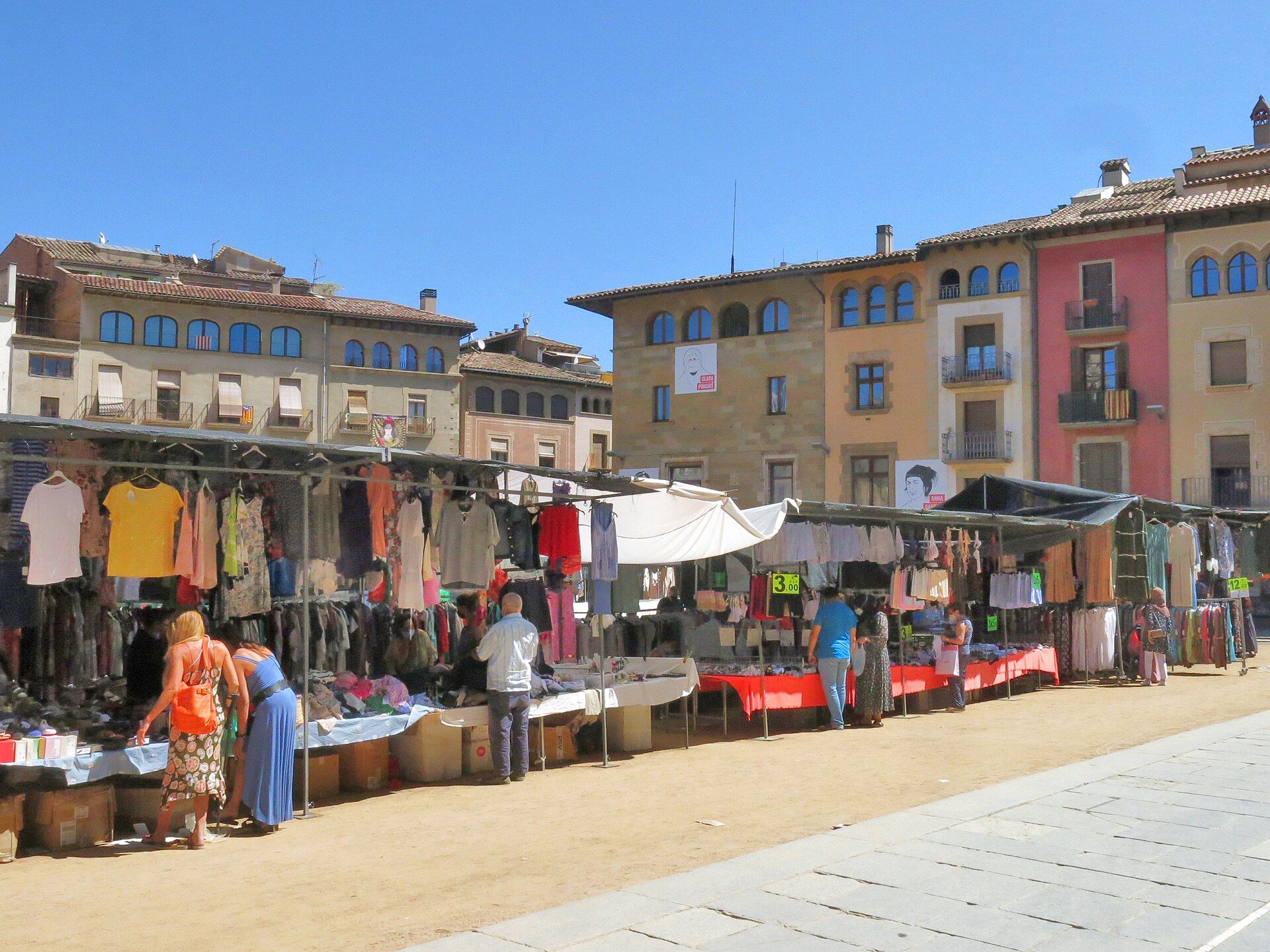 Clothing stalls and shoppers at the Tuesday market on the sandy Plaça Major in Vic, with arcaded town houses behind