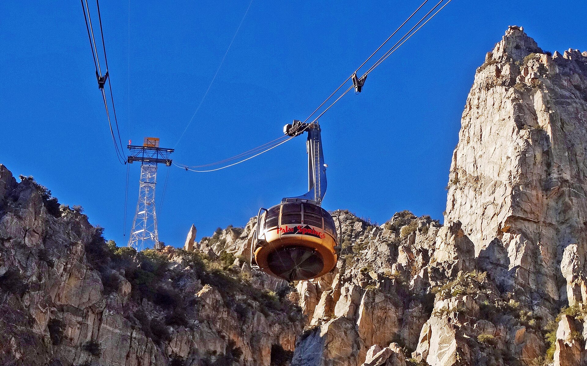 Two aerial tram cars passing each other on the cables above a rocky desert canyon