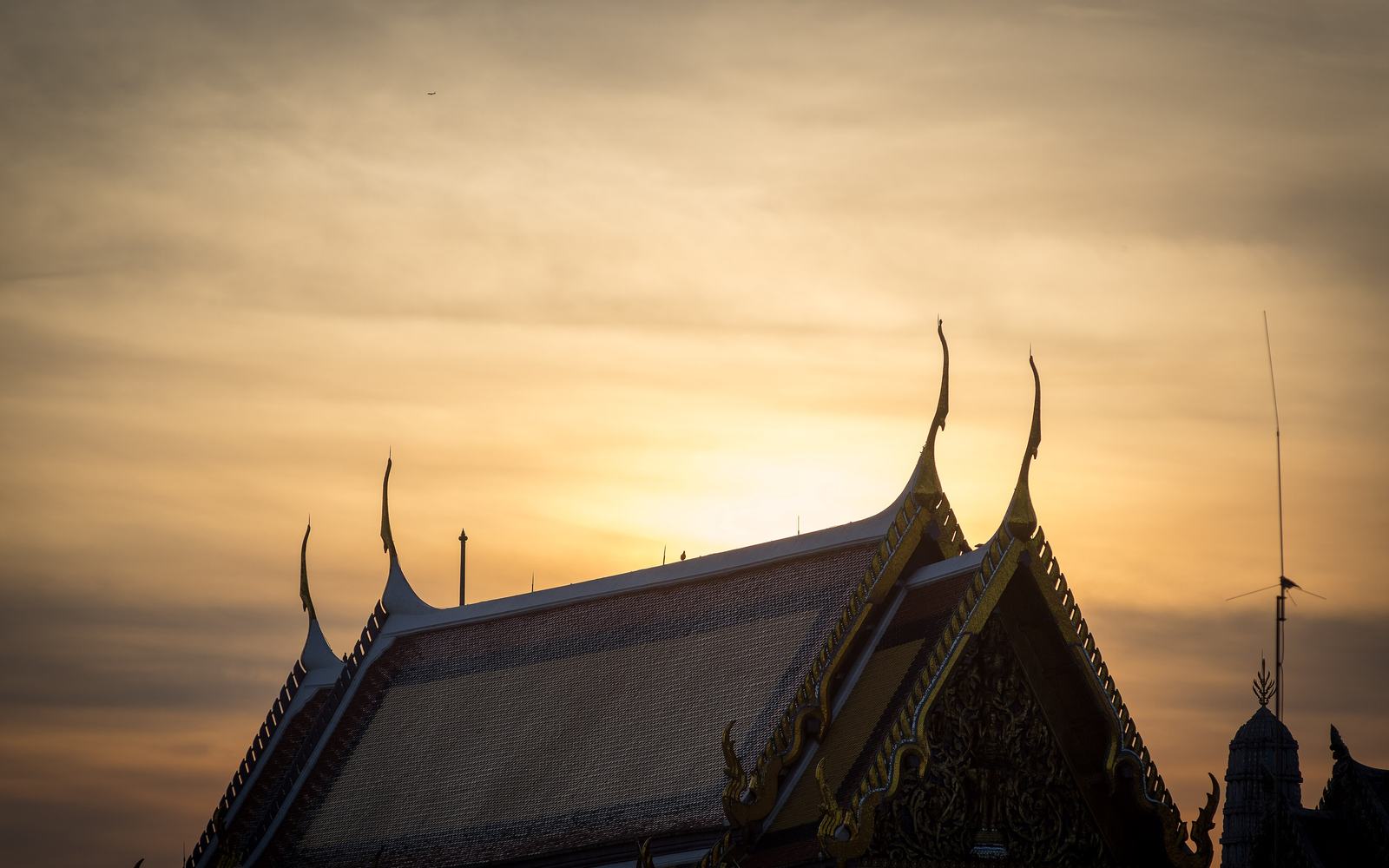 Chofa finials on a Grand Palace roof against a hazy Bangkok sunrise
