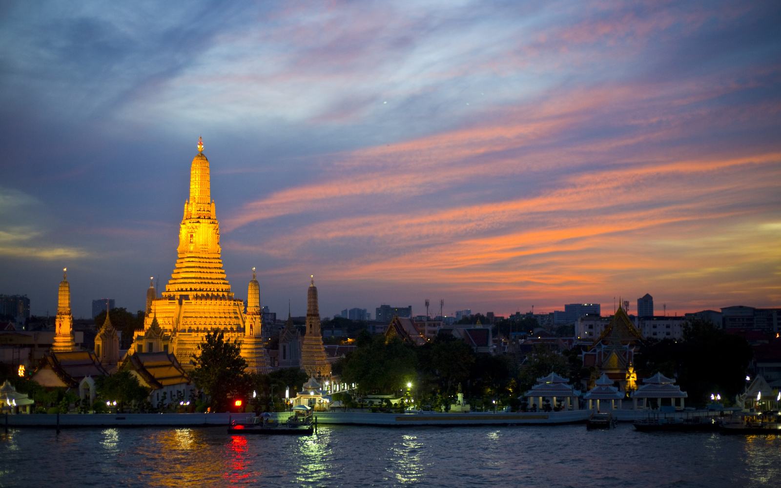 Wat Arun lit gold above the Chao Phraya river at dusk