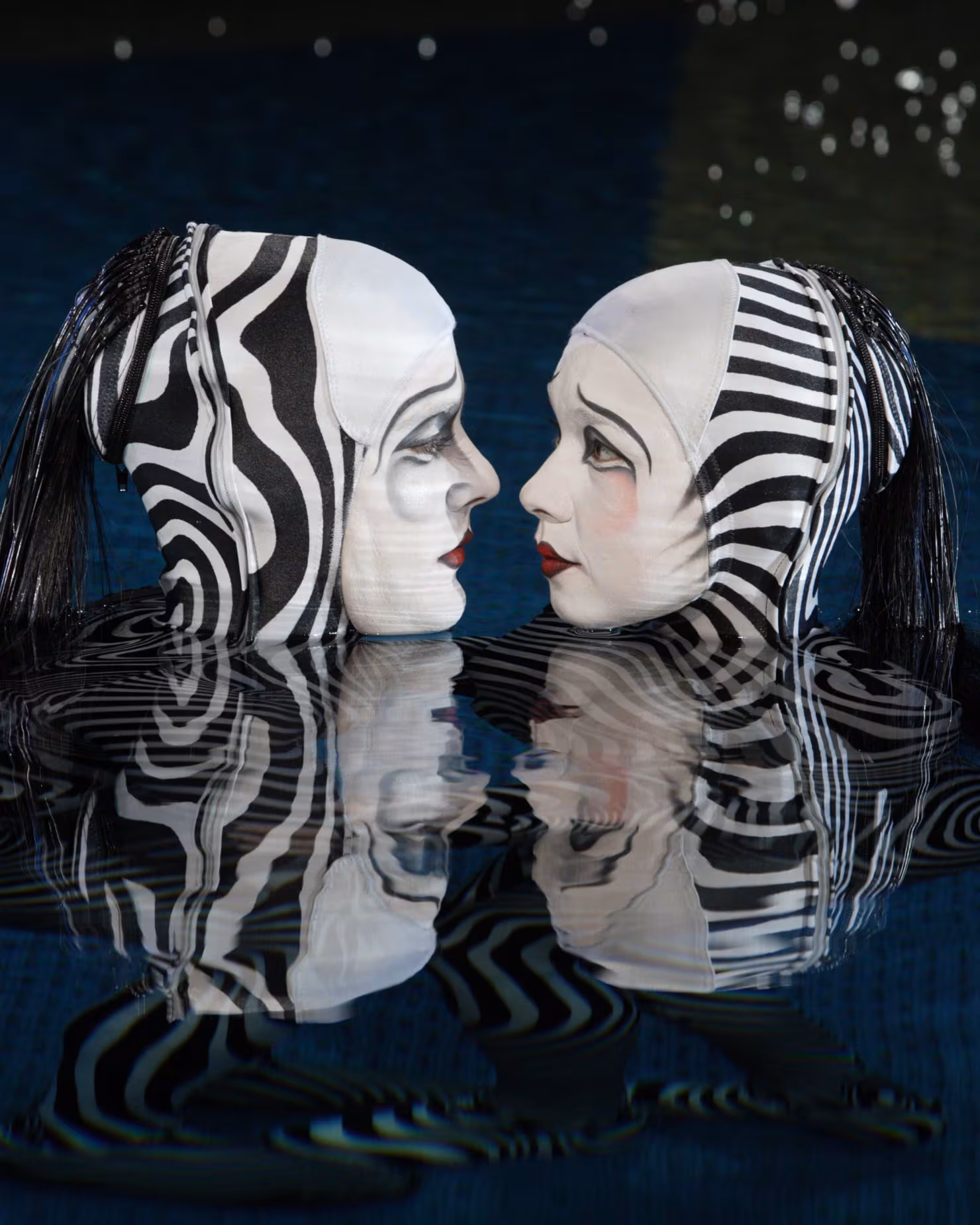 Two performers in mirrored black and white face paint, reflected in the water in “O”